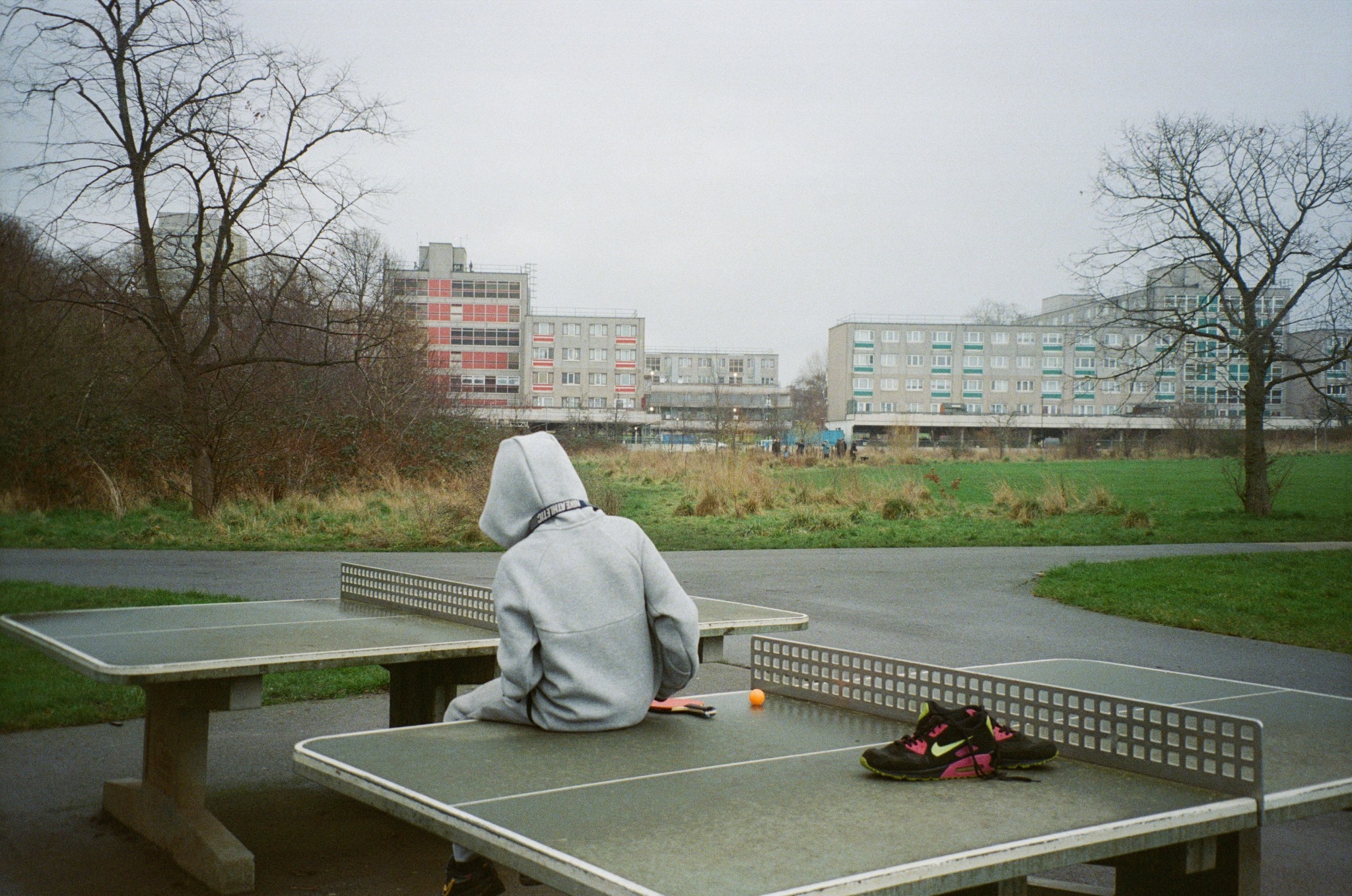 Person seated at an outdoor table tennis court with housing in the background